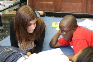 Student teacher and elementary school student sit on the classroom floor, reading