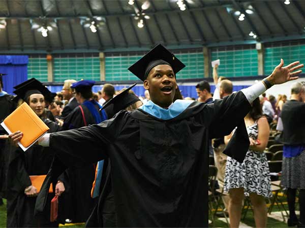 male graduate in a cap and gown throws his hands up excitedly