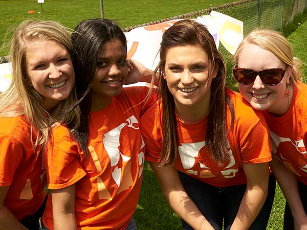 four female students in orange shirts pose outside of a school